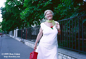 A smiling old woman in a white dress and red accessories walks up the elegant Andrasszy Street in Budapest, Hungary.