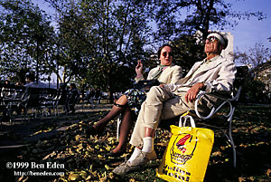 A middle-aged couple enjoys fall afternoon sun sitting on a bench, next to their yellow Julius Meinl shopping bag, on the Danube embankment in Budapest, Hungary.