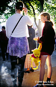 Two teenage girls, one holding a yellow teddy bear backpack stand in whirling dust raised by the crowd of fans during the 1996 European Championship in the Tivoli park, Copenhagen, Denmark.