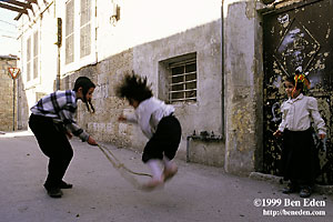 A Jewish orthodox girl jumps across a rope swung by a boy in a kippa with side locks (payot) while another girl watches the play in a secluded street in Mea Shearim, Jerusalem, Israel