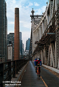 An american cyclist on a road bike wearing a Specialized helmet and reflective clothes traverses the Queensboro Bridge in New York, USA in the direction of Queens