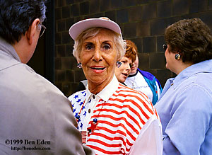 An american middle-aged woman - possibly a war veteran - wearing an americana-clad shirt, necklace, hat and heart-shaped earrings, waiting in line to board the USS Intrepid Aircraft Carrier Museum on a Memorial Day in Manhattan, New York