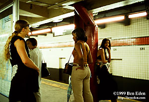 An attractive young black woman stands with her hand in her back pocket while two bystanders watch her in the42-nd Street Subway Station in Manhattan, New York