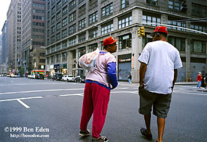 Two black pedestrians dressed in sports clothes and wearing red caps hesitatingly cross an empty downtown Manhattan avenuein New York City