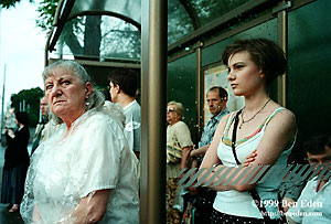 Streetcar passengers - an attractive teenager and an old woman wearing a transparent polyethylene raincoat - wait at a tram stop in Karlovo Square, Prague, Czech Republic