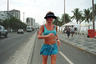 A middle-aged blonde woman in bikini-top jogs along Ipanema beach, Rio de Janeiro, Brazil