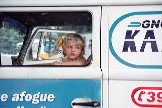 A blonde, blue-eyed little girl presses her nose on the window pane as she waits in a vintage Volkswagen van parked by the Copacabana beach in Rio de Janeiro, Brazil