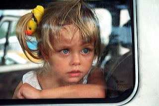A blonde, blue-eyed little girl with a yellow duck tie in her hair presses her nose on the window pane as she waits in a vintage Volkswagen van parked by the Copacabana beach in Rio de Janeiro, Brazil