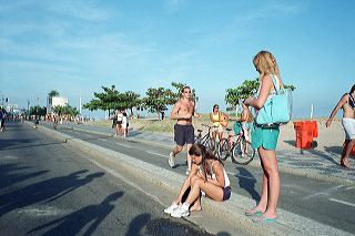 A Sunday afternoon scene on Ipanema beach, Rio de Janeiro. A female is adjusting her shoes while a male jogger passes by