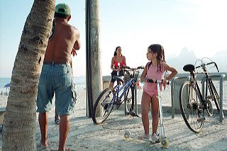 Little girl wearing a pink T-shirt stands on her collapsible scooter and looks towards the Ipanema beach in Rio de Janeiro, Brazil  